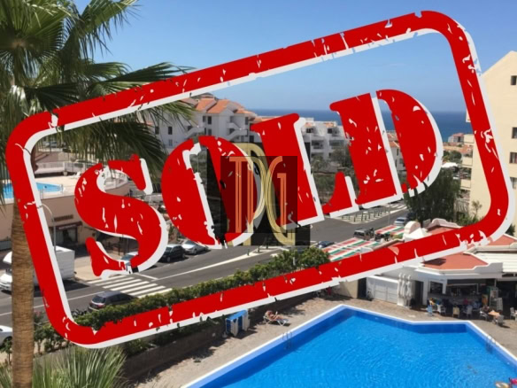 Resort-style pool area with palm trees and white buildings, overlaid by a large red 'SOLD' stamp indicating the property is sold.