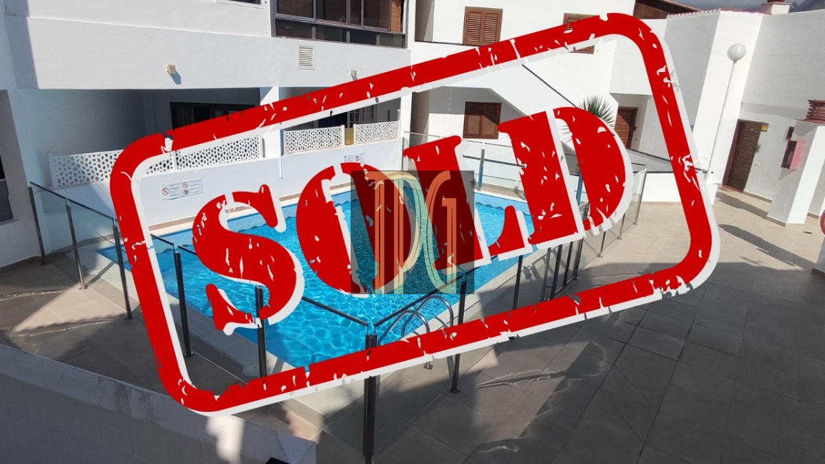 SOLD 1 Outdoor pool area in a white building complex with glass railings; a bold red 'SOLD' stamp overlays the scene.