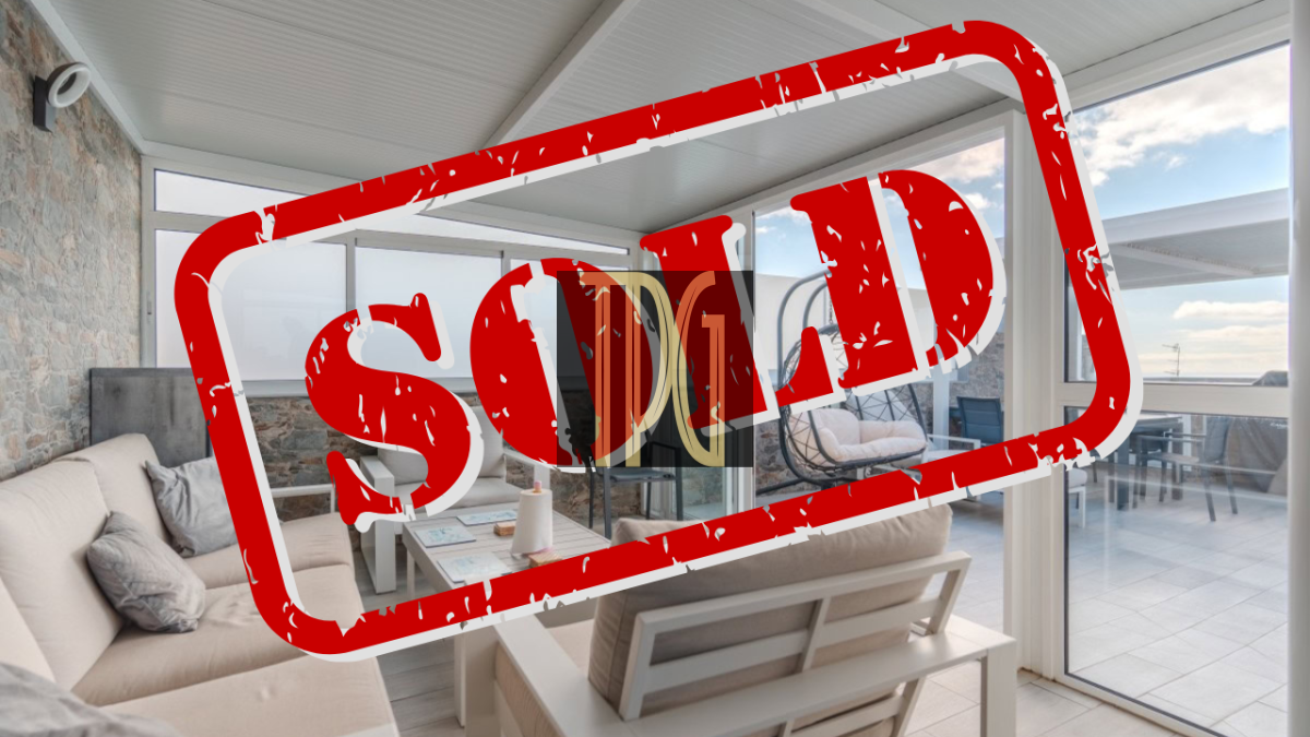 Bright modern living room with beige sofa and large windows, a red SOLD stamp across the scene.