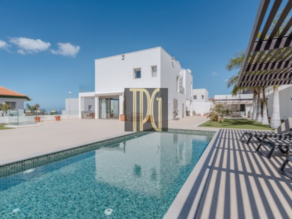 Outdoor pool in a modern white villa complex with sun loungers and palm trees under a clear blue sky.