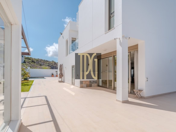 White modern house with a large glass-door patio, pool in the background, under a bright blue sky.