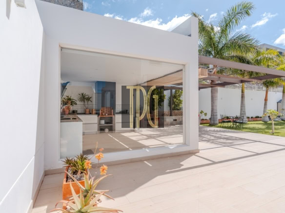White modern house with a large glass door opening to an outdoor kitchen and patio, sunny day with palm trees in the yard