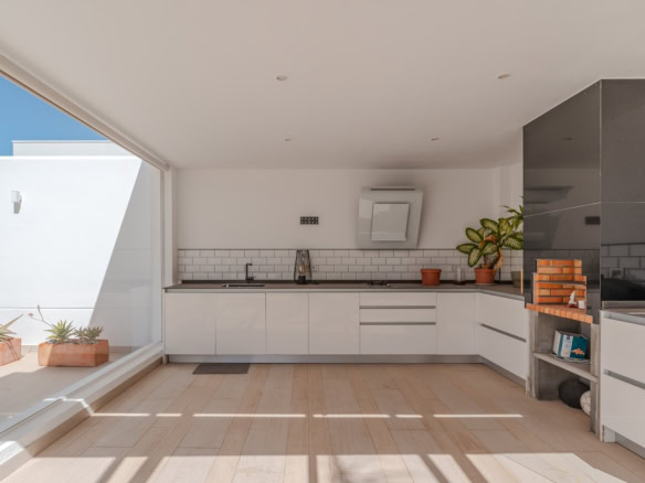 Bright modern kitchen with white cabinets, black countertops, and a large sliding door opening to an outdoor patio with potted plants in terracotta pots.