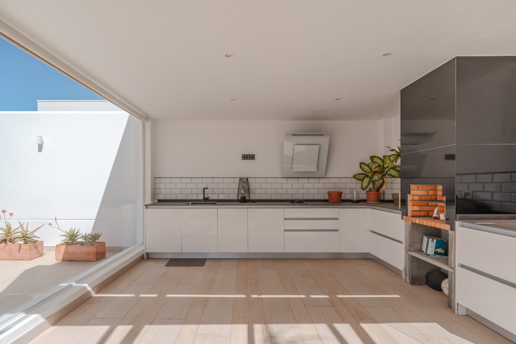 Bright modern kitchen with white cabinets, black countertops, and a large sliding door opening to an outdoor patio with potted plants in terracotta pots.