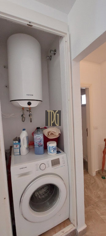 Tall white water heater mounted in a small closet above a front-loading Samsung washing machine; detergent bottles and a towel on the washer.