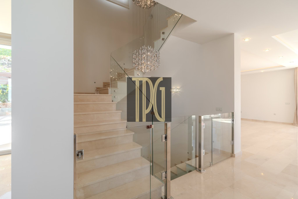 Modern two-story foyer with a beige marble staircase, glass railings, and a crystal chandelier.