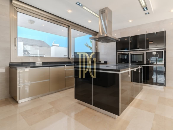 Modern kitchen with a black glossy island, stainless steel range hood, and built-in ovens along a wall of matching cabinets.