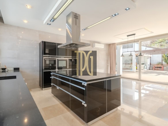 Modern kitchen with a glossy black island, stainless range hood, and built-in ovens; large glass doors to outdoor patio nearby.