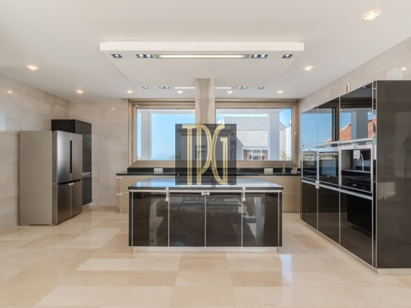 Modern, spacious kitchen with a large central island, glossy black cabinets, and stainless steel appliances including a tall fridge and double ovens, facing a wide window.