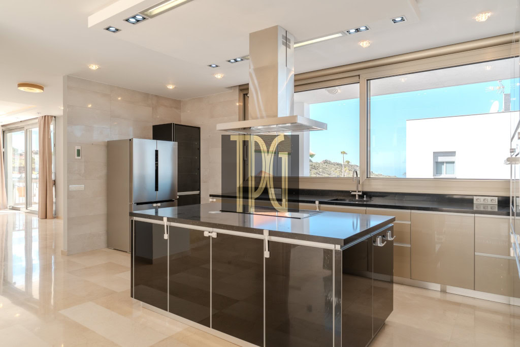 Modern kitchen with a black island, stainless steel refrigerator, and a large windowed wall showing outdoor light.