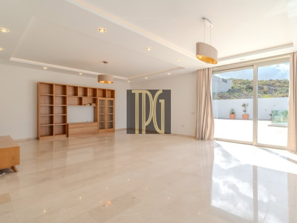 Spacious modern living room with a large wooden bookshelf, recessed ceiling lights, and glass sliding doors to a sunny patio outside.