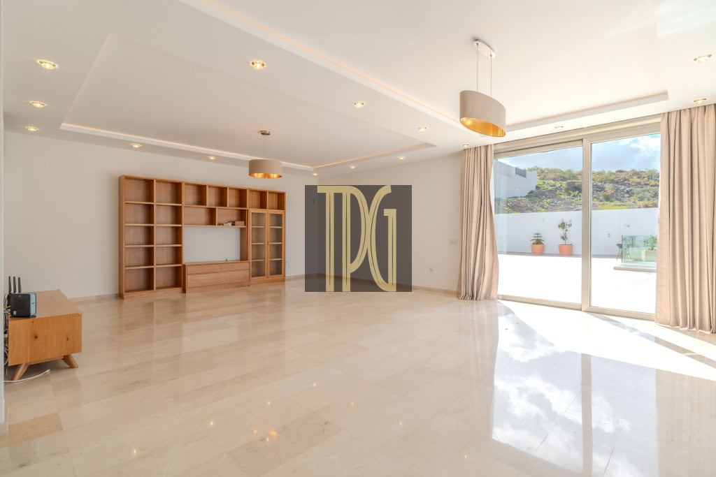 Spacious modern living room with a large wooden bookshelf, recessed ceiling lights, and glass sliding doors to a sunny patio outside.