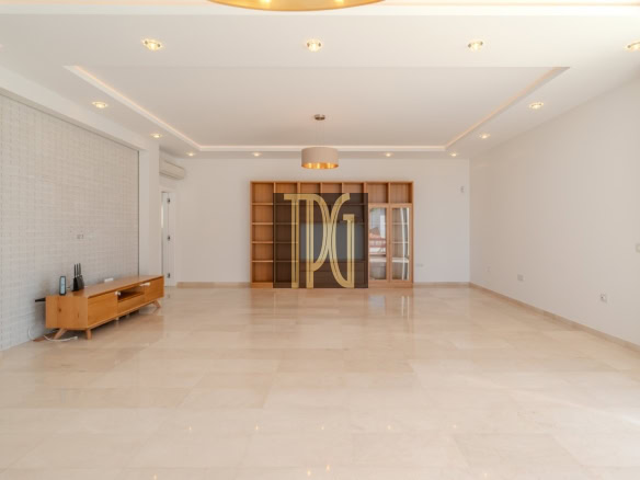 Spacious modern living room with beige marble floor, built-in wooden bookshelf, TV stand, and large windows with curtains.