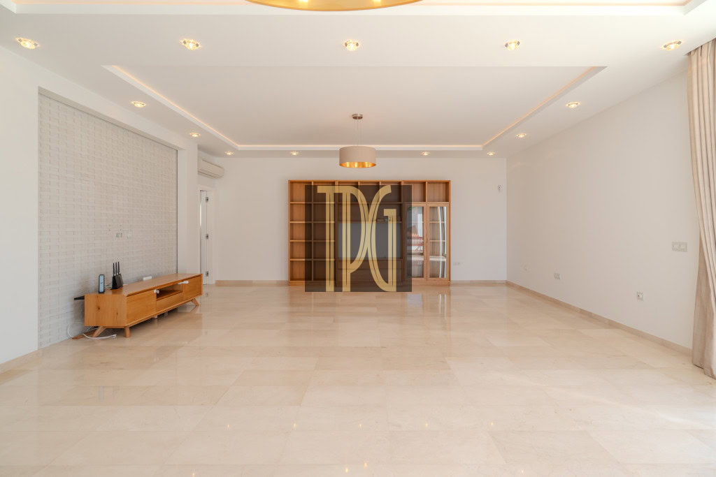 Spacious modern living room with beige marble floor, built-in wooden bookshelf, TV stand, and large windows with curtains.