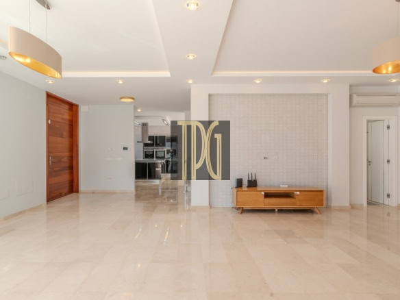 Empty modern living room with beige marble floor, wooden door on the left, and a low wooden TV console against a tiled wall in the center.