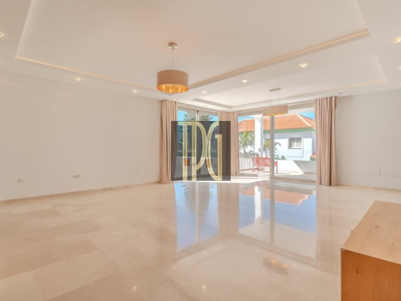 Spacious modern living room with beige tiled floor, white walls, and large sliding glass doors to a sunlit patio.