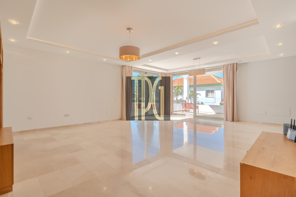 Spacious modern living room with beige tiled floor, white walls, and large sliding glass doors to a sunlit patio.