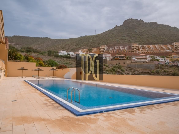 Rectangular blue pool in a resort courtyard with tan tile deck and beige walls, mountains in the background