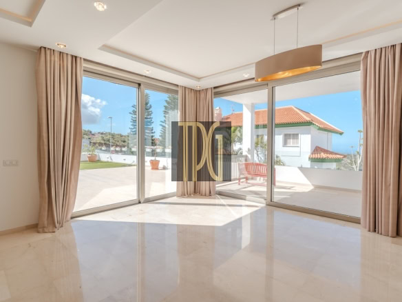 Sunlit living room with large glass sliding doors opening to a patio, beige curtains, and a polished tile floor.