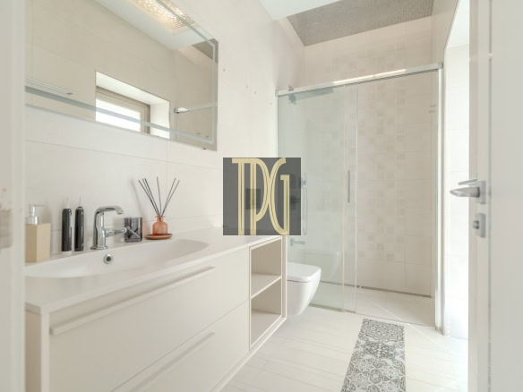 Bright modern bathroom with a white vanity, sink, and mirror, plus a toilet and glass shower enclosure.