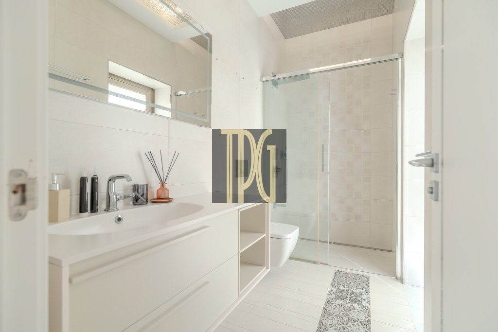 Bright modern bathroom with a white vanity, sink, and mirror, plus a toilet and glass shower enclosure.