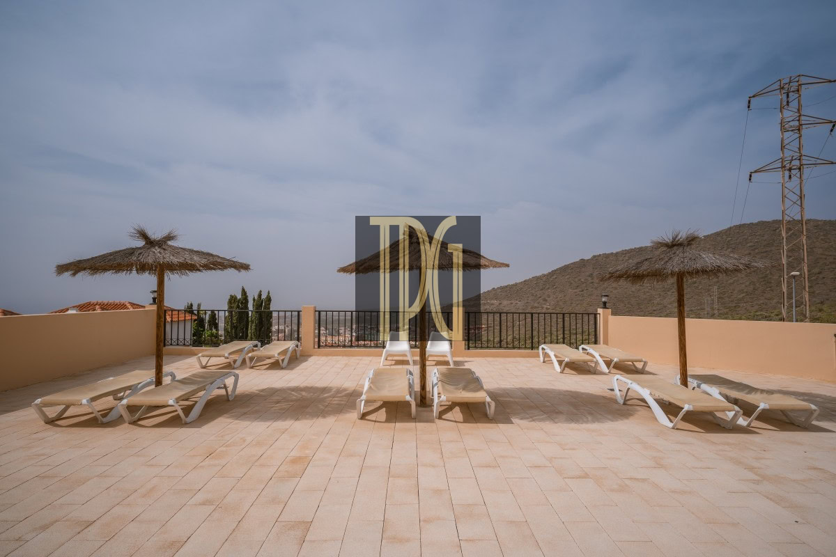Sun loungers on a tiled terrace with thatched umbrellas and a railing overlooking hills and clear sky.