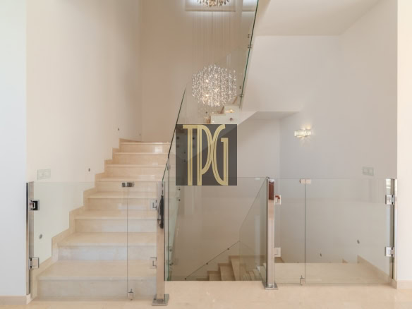 Modern white staircase with glass balustrade and chandelier in a bright interior space.