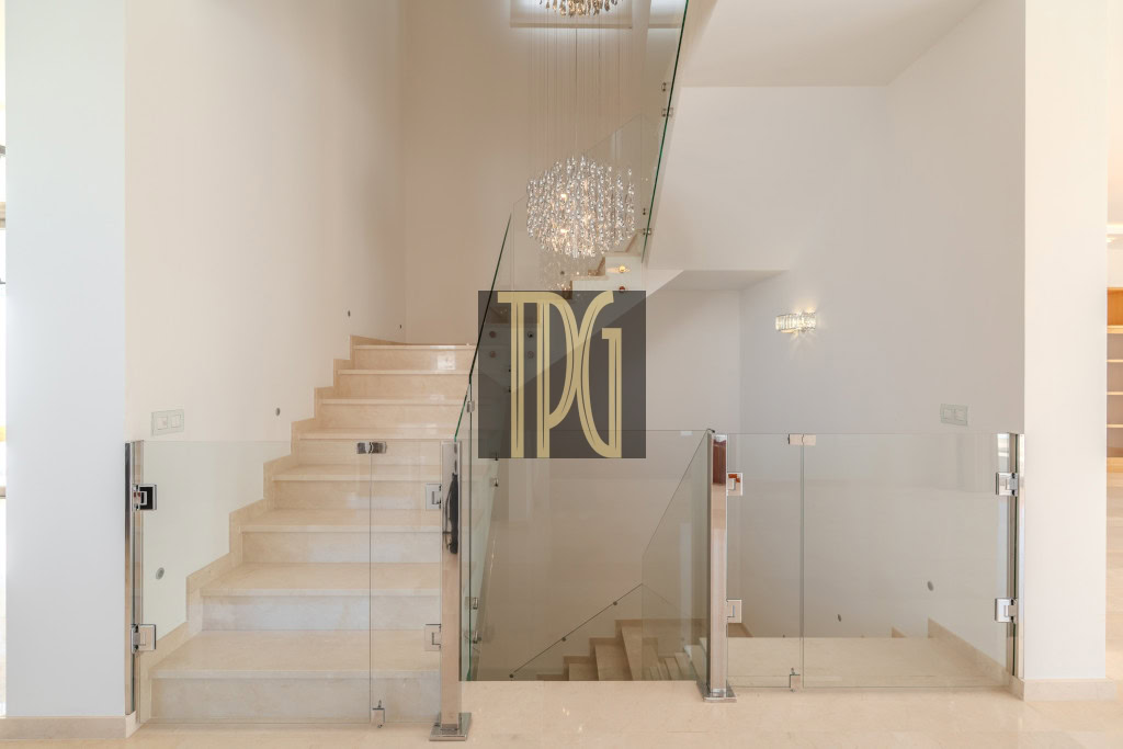 Modern white staircase with glass balustrade and chandelier in a bright interior space.