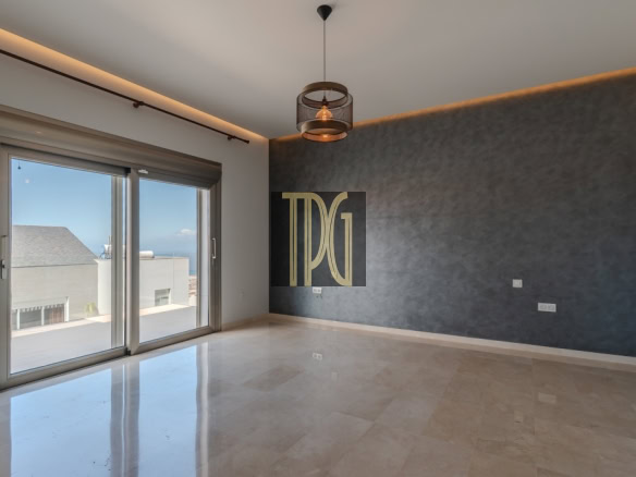 Modern empty living room with a textured dark blue accent wall, large sliding glass doors to a balcony, and a circular pendant light hanging from the ceiling.