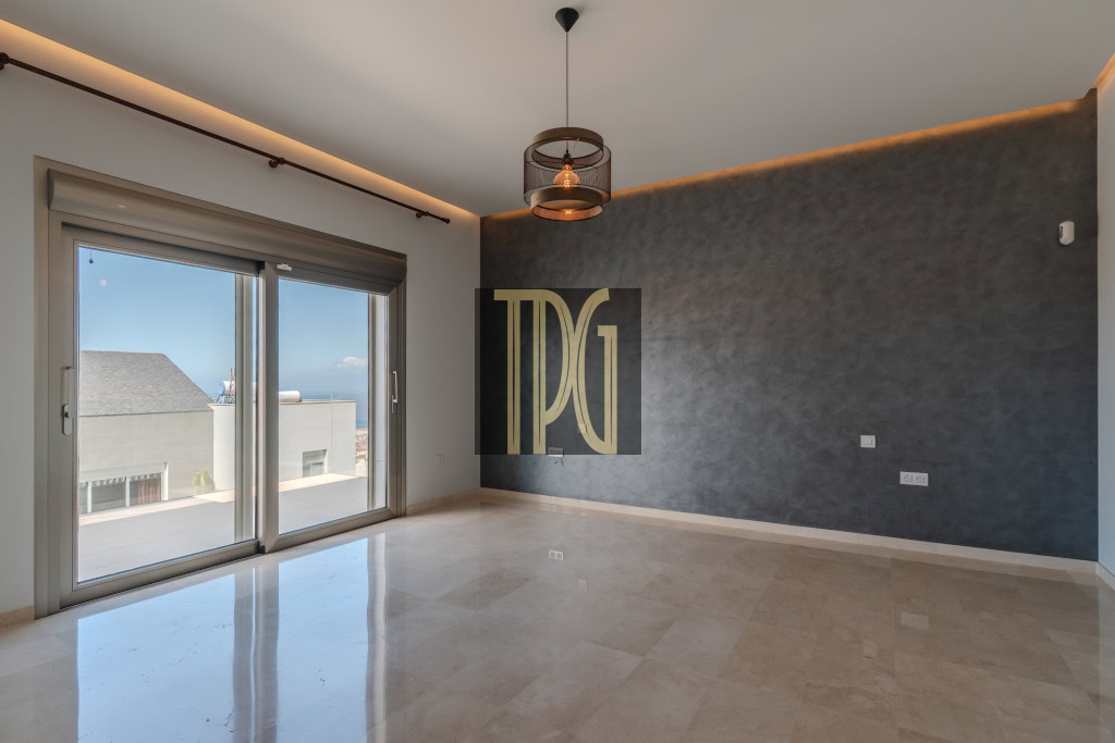 Modern empty living room with a textured dark blue accent wall, large sliding glass doors to a balcony, and a circular pendant light hanging from the ceiling.