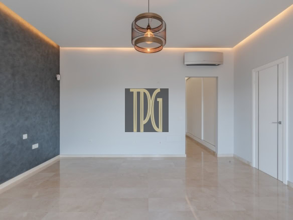 Empty modern living room with a dark textured feature wall on the left, white walls, and beige tiled floor; doorway to a hallway visible in back.