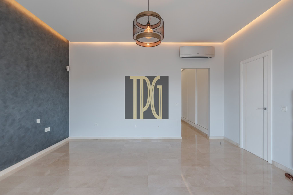 Empty modern living room with a dark textured feature wall on the left, white walls, and beige tiled floor; doorway to a hallway visible in back.