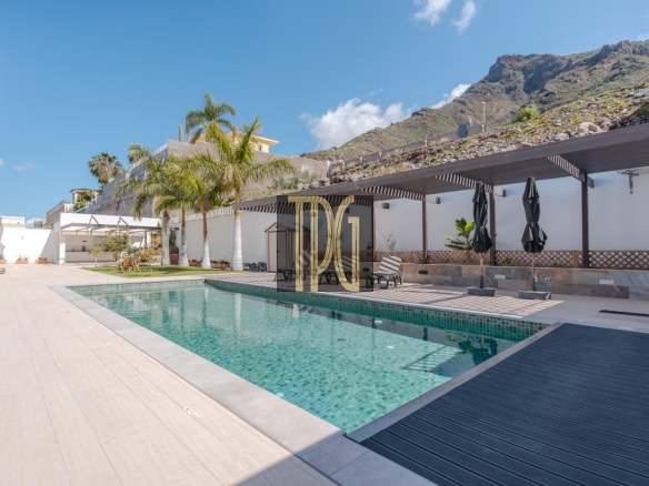 Outdoor pool area at a sunny resort with palm trees, lounge chairs, and shaded seating under a pergola.