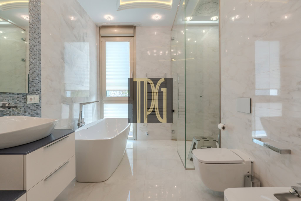 Modern white bathroom with a freestanding tub, double vanity, glass shower, and wall-mounted toilet.
