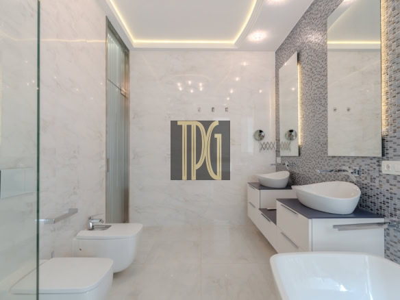 Modern white bathroom with a glass shower, bidet and toilet on the left, and a floating vanity with two vessel sinks along a mosaic-tiled wall on the right.