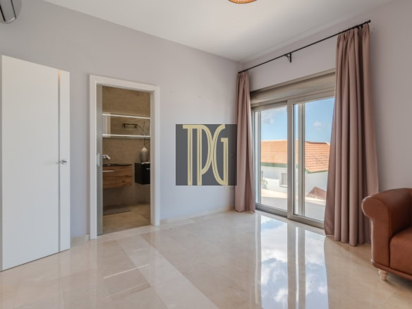 Bright living room with a large sliding glass door to a balcony, pink curtains, and a brown leather sofa; an open doorway reveals a closet area on the left.