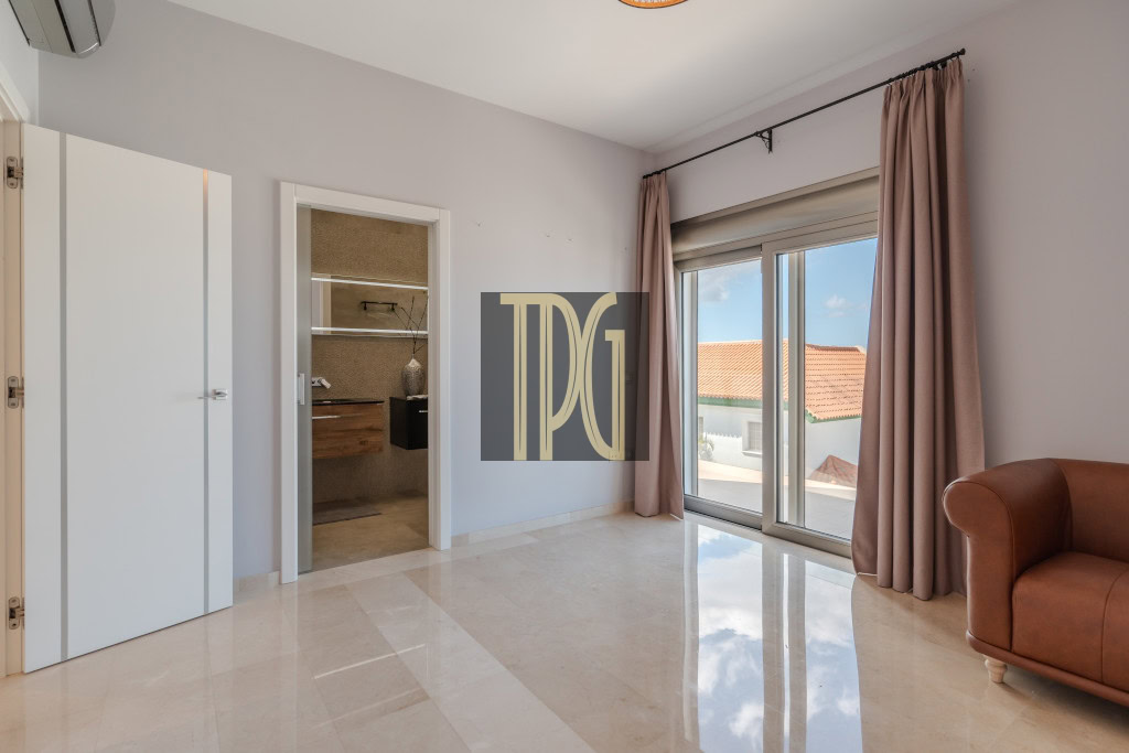 Bright living room with a large sliding glass door to a balcony, pink curtains, and a brown leather sofa; an open doorway reveals a closet area on the left.