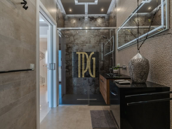 Modern bathroom with glass shower door featuring a large gold TDG logo; black countertop and decorative vase nearby