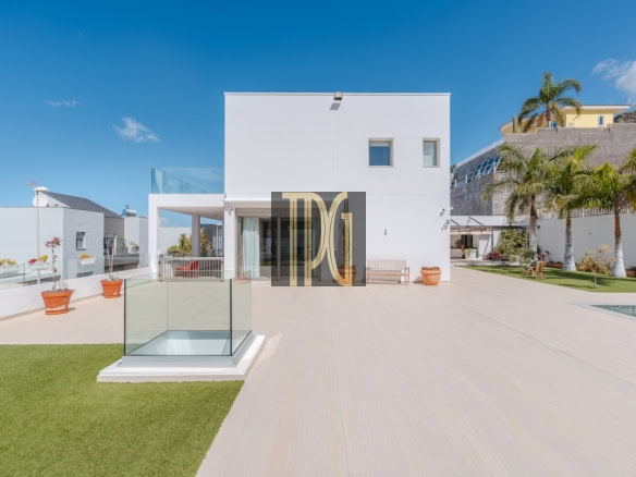 Modern white villa with a spacious terrace, glass railing, and palm trees under a bright blue sky.