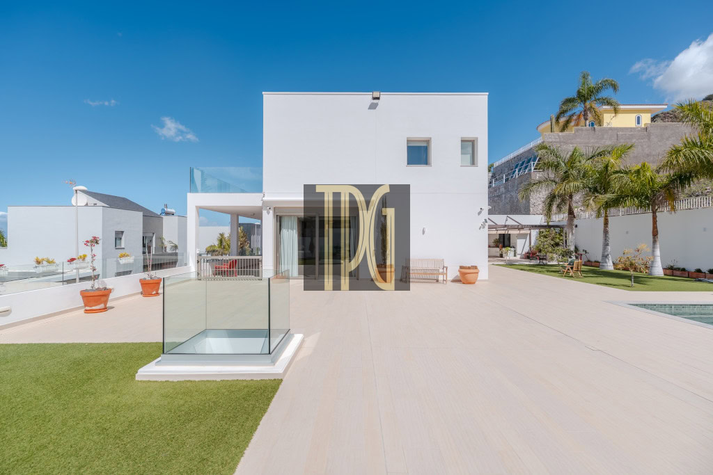 Modern white villa with a spacious terrace, glass railing, and palm trees under a bright blue sky.