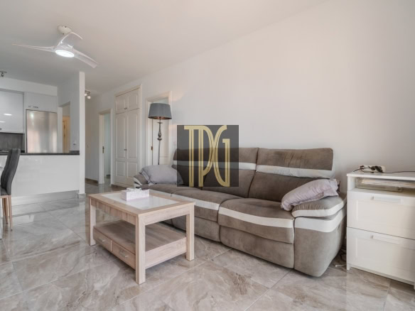 Cozy living room with beige sectional sofa, wooden coffee table, and white side drawers next to a window with patterned curtains.