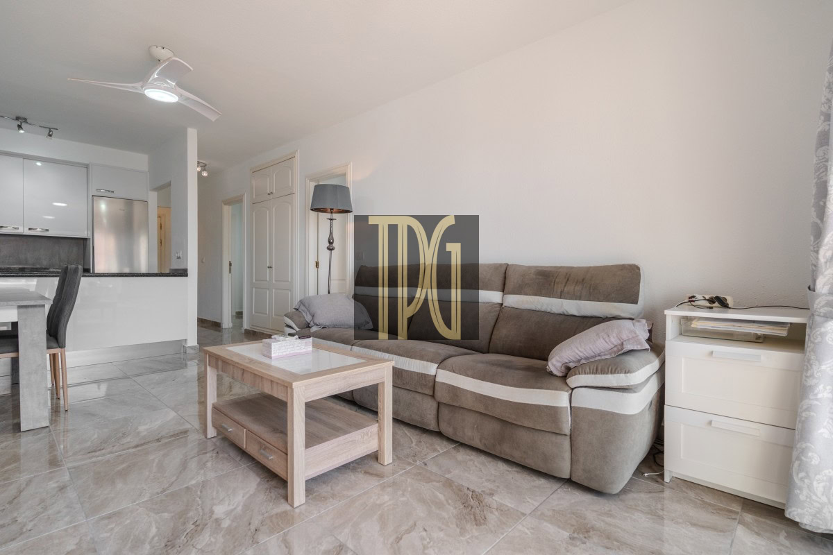Cozy living room with beige sectional sofa, wooden coffee table, and white side drawers next to a window with patterned curtains.
