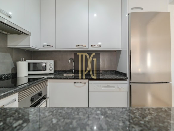 Modern white kitchen with granite countertops, a microwave, sink, dishwasher, and a stainless steel fridge.