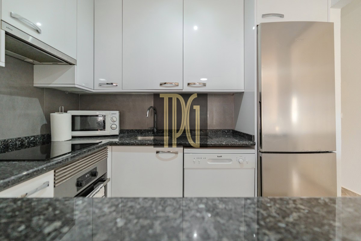 Modern white kitchen with granite countertops, a microwave, sink, dishwasher, and a stainless steel fridge.