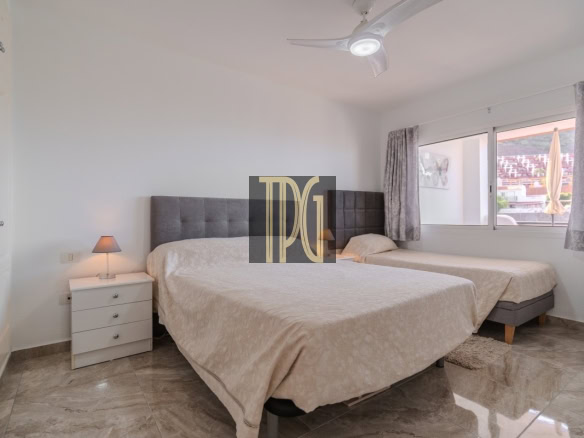 Twin-bed setup with shared padded headboard, white nightstand and lamp between beds in a bright hotel room.