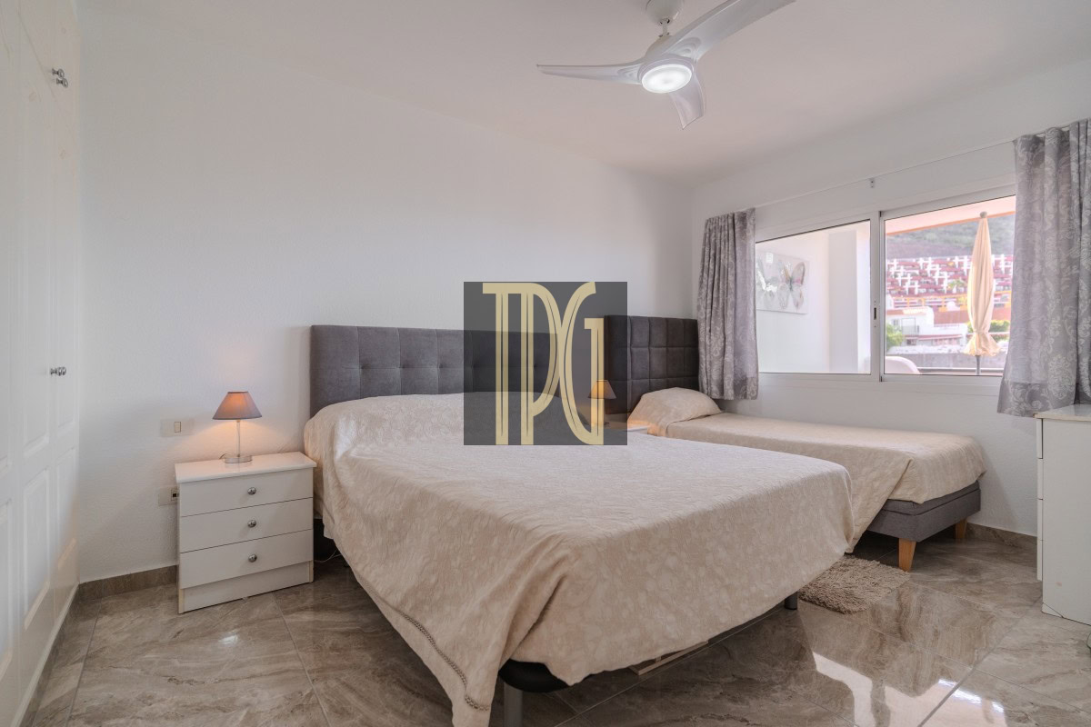 Twin-bed setup with shared padded headboard, white nightstand and lamp between beds in a bright hotel room.