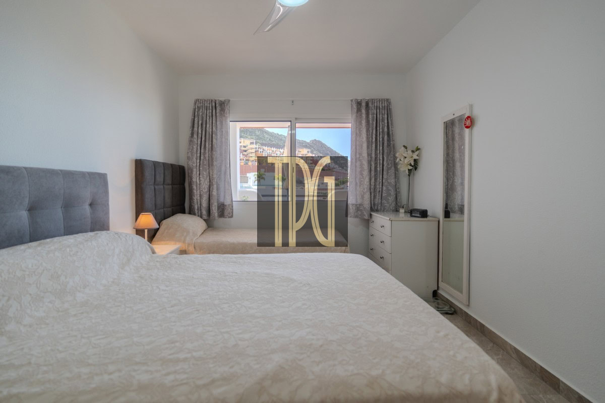 Hotel bedroom with two twin beds and grey tufted headboards; window view of buildings and hills, dresser with flowers and a full-length mirror nearby.