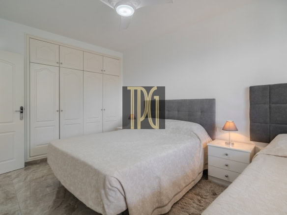Bedroom with two beds and gray tufted headboards, white nightstand between them, and a large white wardrobe along the wall.