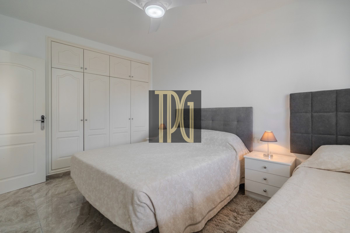 Bedroom with two beds and gray tufted headboards, white nightstand between them, and a large white wardrobe along the wall.
