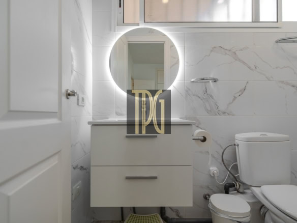 Circular backlit mirror above a white two-drawer vanity in a modern marble-tiled bathroom